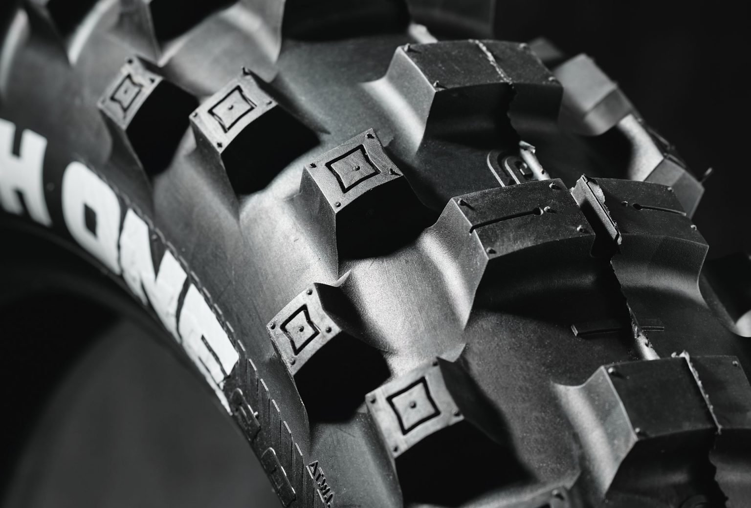 Super close up of a brand new 'The Tough One' Plews Tyre enduro tire in a black studio environment. Detail shot of the treads and sidewall lettering.