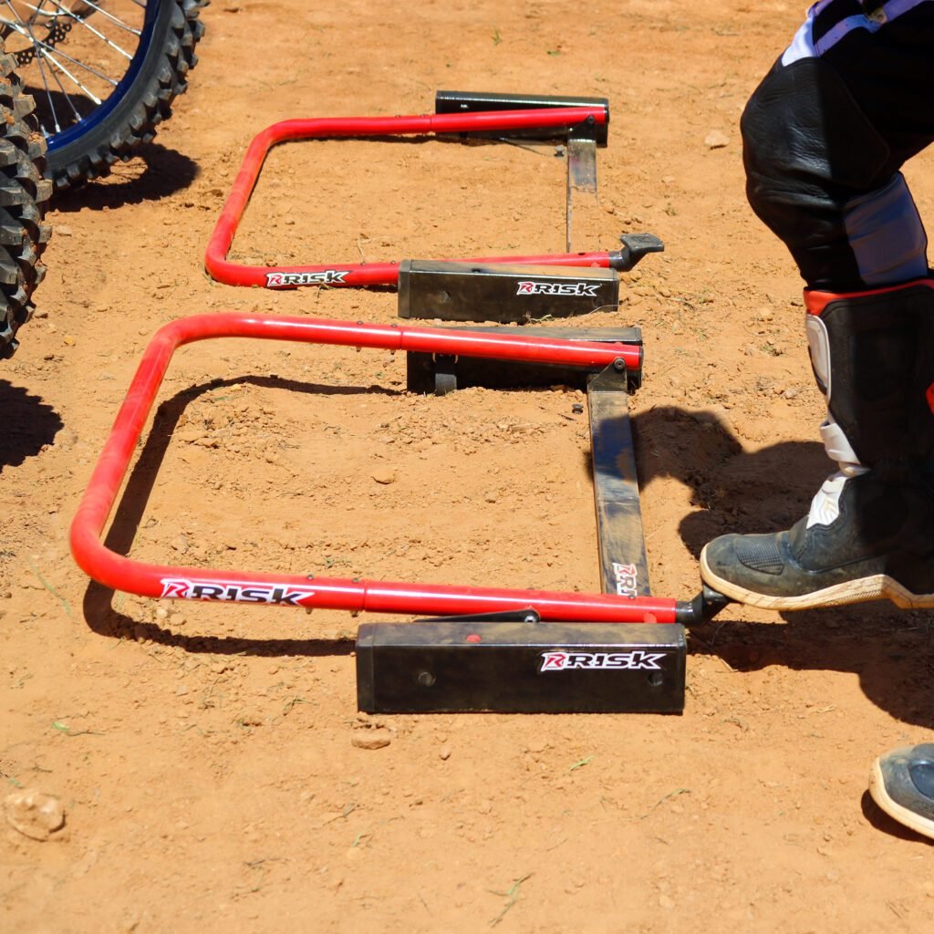Two Holeshot Pro gates laying in the down position. A persons foot just about to engage the foot petal to reset one of the gates.